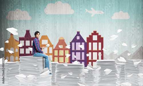 Young man sitting on pile of paper documents.