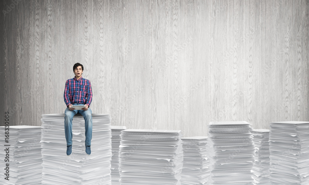 © adam121 - Attractive man sitting on pile of paper documents.