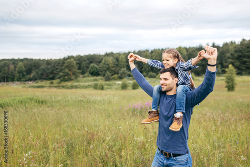 Happy cute daughter piggybacking on her father to see beautiful nature while having stroll together. Handsome young dad and his little child playing on nature. Father showing something to his daughter