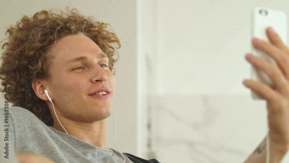 Young cheerful man in headphones making videocall on smartphone and talking to somebody at home
Young cheerful man in headphones making videocall on smartphone and talking to somebody at home