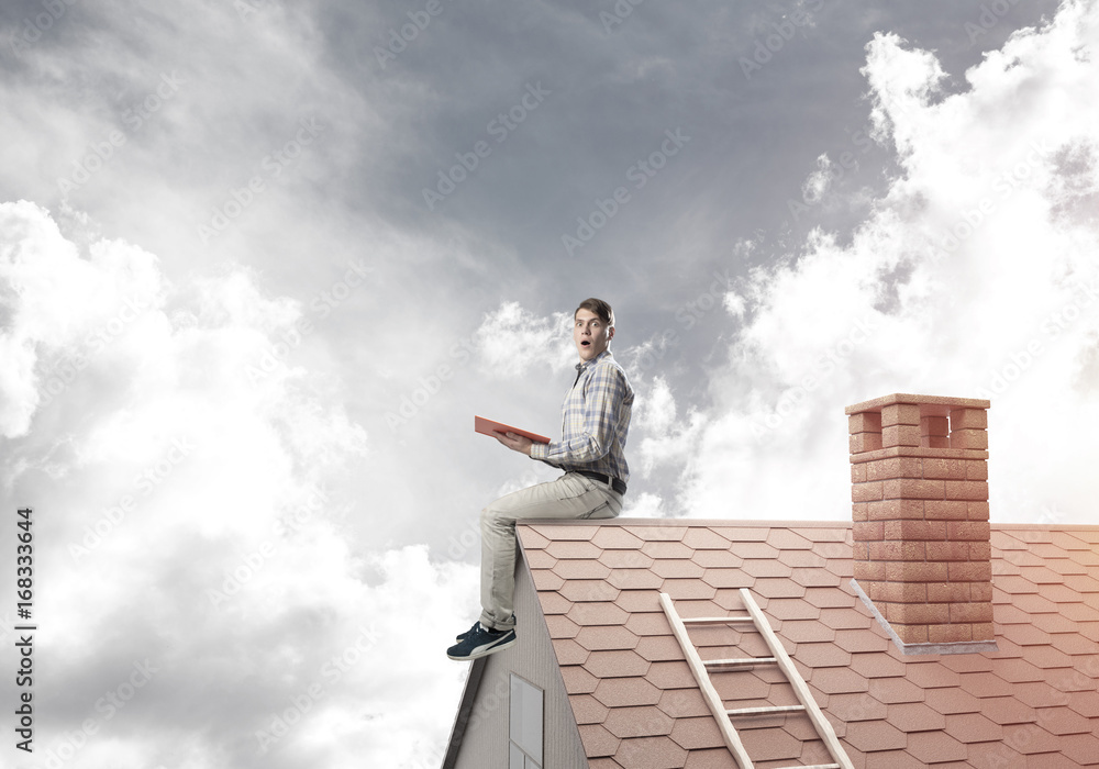 Handsome man on brick roof against cloud scape reading book Handsome man on brick roof against cloud scape reading book