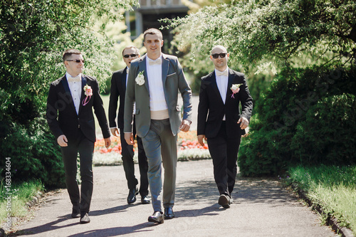 Groom and his groomsmen in black suits walk along the road