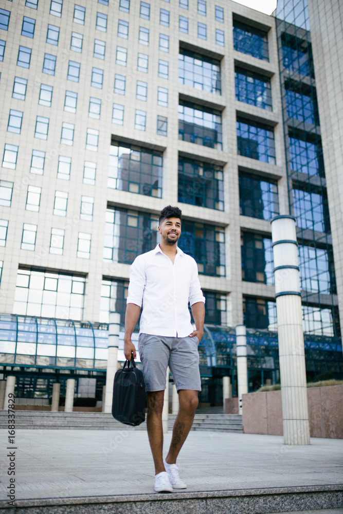 Young handsome Afro American man standing in front of huge modern business building Young handsome Afro American man standing in front of huge modern business building