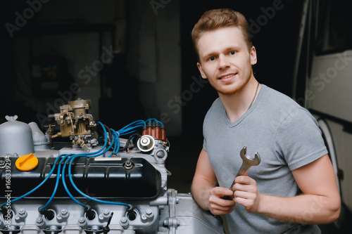 A close-up of an auto mechanic smiling repairs the engine of a lorry or bus replacement of a candle, a concept repair in a garage, a workshop.