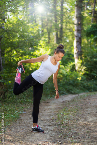 Young female fitness model stretching in the woods