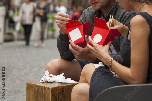 Young Woman and man Eating Asian wok Noodle Cuisine Chinese food from Take away Box Wok Box at the urban street background