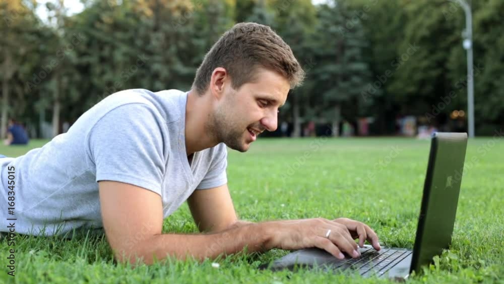 A young man in the park is working behind a laptop. Mobile office, freelancer. A young man in the park is working behind a laptop. Mobile office, freelancer.