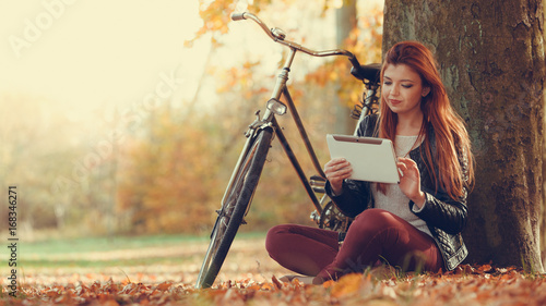 Girl is sitting under the tree with tablet.