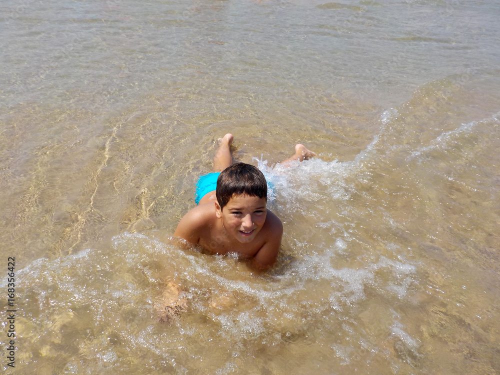 A boy enjoing cool water of mediterranian sea on the beach of spanish coast