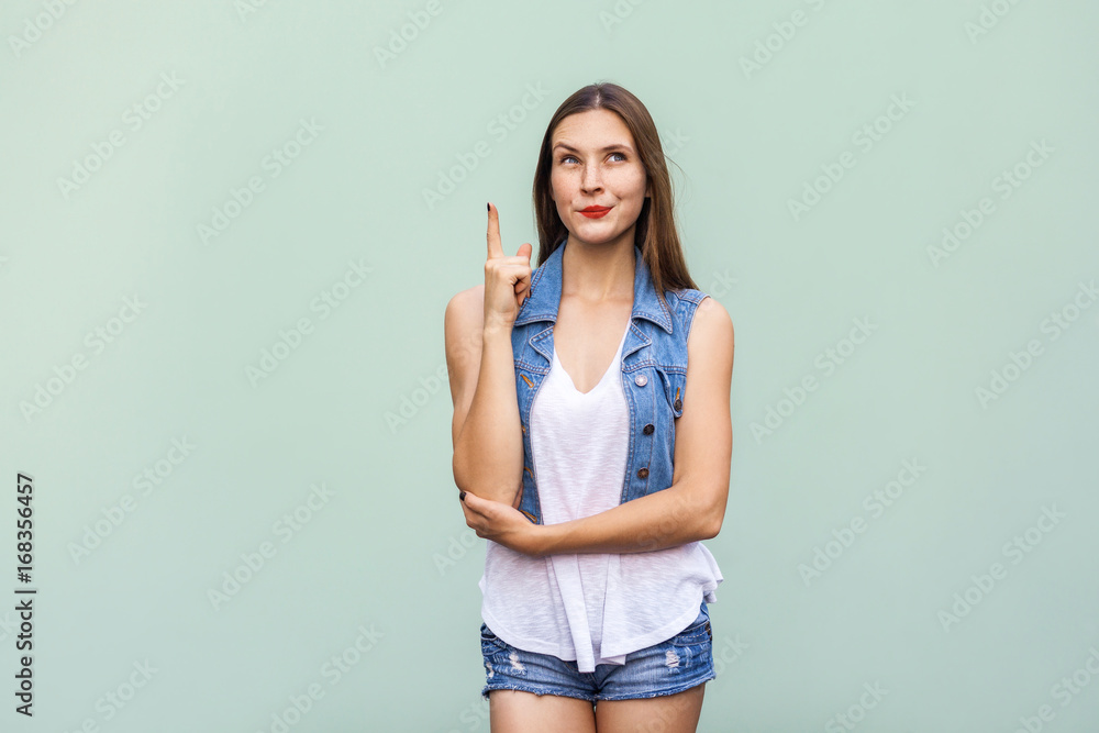 The tender and cute teenage female with shy faint smile, freckles and and clean skin, got the idea and she raised her finger up and looking up. Isolated studio shot on light green background The tender and cute teenage female with shy faint smile, freckles and and clean skin, got the idea and she raised her finger up and looking up. Isolated studio shot on light green background