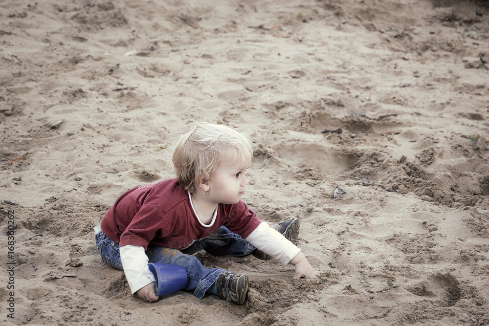 Happy baby girl, toddler, playing with sand on a playground.