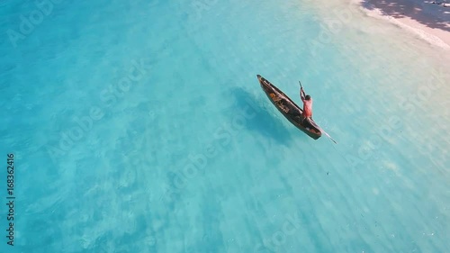 Aerial view of a poor fisherman with a torn shirt sails on a small boat on clear blue water along a tropical beach with beautiful hotels in Africa. Indian Ocean. Zanzibar. 2017