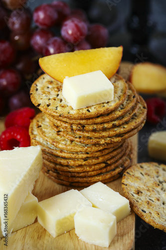 Cheddar cheese, creckers and fruits on wooden board photo