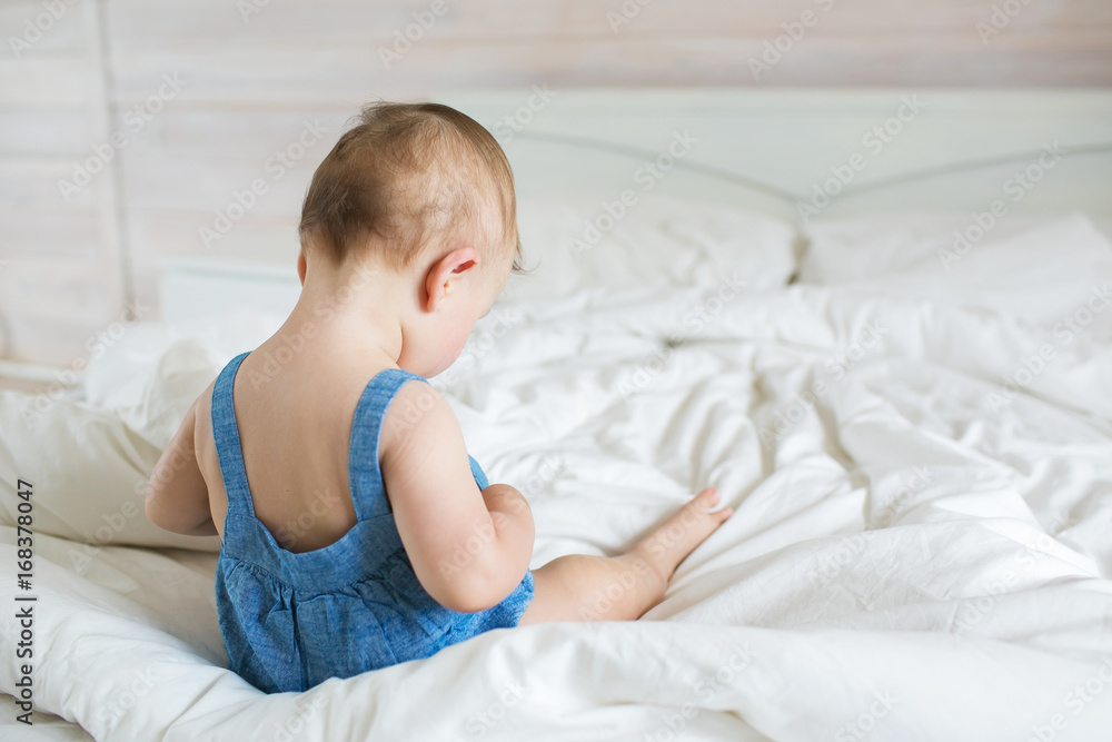 Back view of a little baby in denim dress sits on a bed Back view of a little baby in denim dress sits on a bed