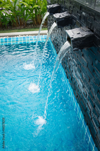 Small waterfall on the wall is streaming to the modern swimming pool beside the house or hotel