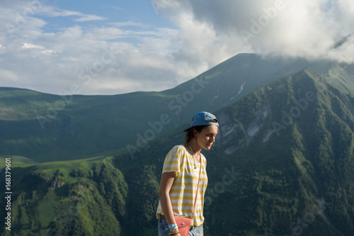 A young girl in a striped yellow T-shirt and a cap in the summer on the fairy-tale mountains and a mysterious misty sky background.