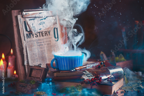 Rising steam in a ceramic tea cup on a wooden background with candles, mystery newspaper clips, books, leaves and moss photo