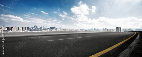 Slika na platnu empty road and cityscape of modern city against cloud sky