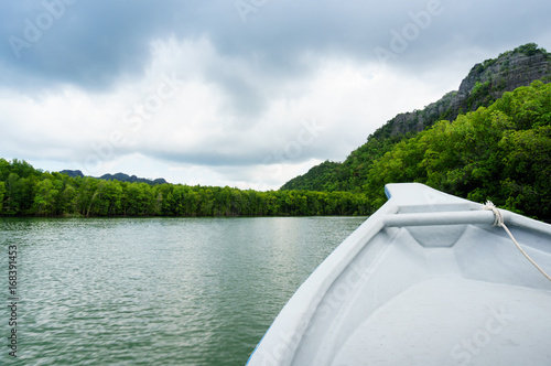 In boat shot during the river cruise showing the tree covered hills, cloudy skies and beautiful green water in in Kilim park Langkawi. This is a popular tourist destination
