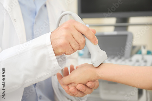Doctor conducting ultrasound examination of woman's wrist in clinic
