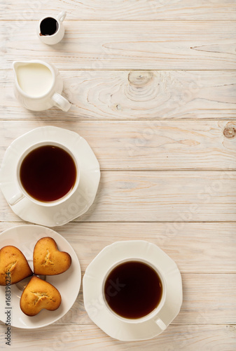 Cups with tea and cupcakes in the shape of a heart on a light wooden background.