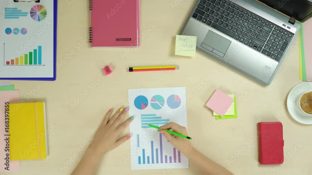 Freelancer working with graphs at workplace, creative person, inspiration, ideas. Top view of a woman checking graphs and typing on laptop Freelancer working with graphs at workplace, creative person, inspiration, ideas. Top view of a woman checking graphs and typing on laptop