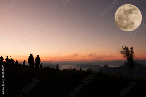 silhouette of people the cliff and looking at the valley and mountain with full moon
