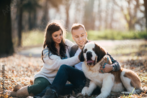 Young couple enjoying nature outdoors together with their adorable Saint Bernard puppy. People and dogs theme. photo