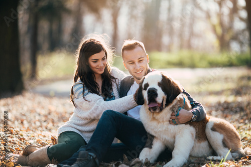 Canvas Print Young couple enjoying nature outdoors together with their adorable Saint Bernard puppy