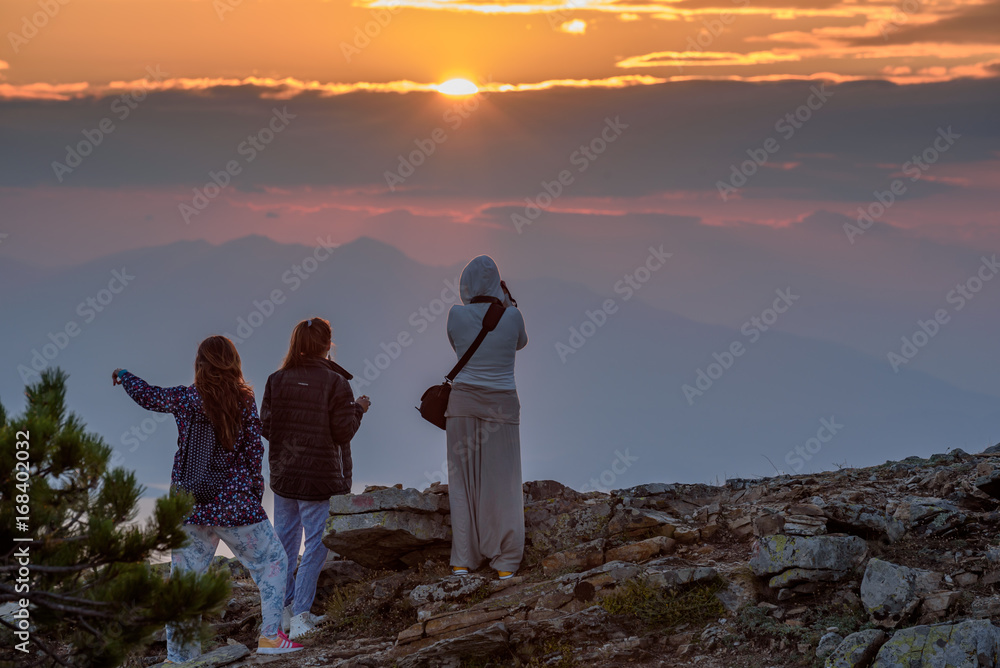 Group of women photographing and enjoying the setting sun on top Ipsarion, Thassos island, Greece - amazing mountain landscape