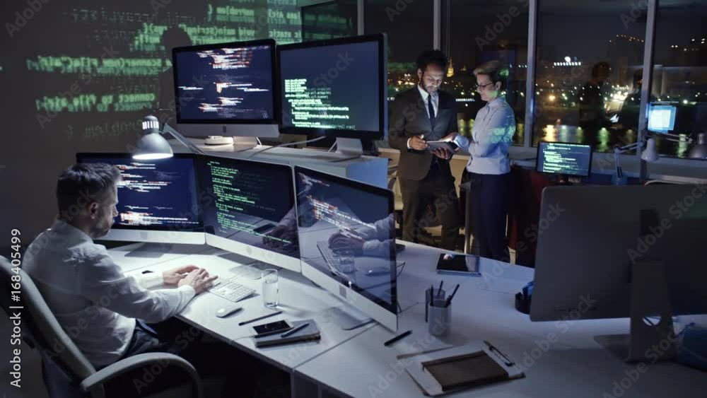 Male programmer typing computer code on multi-screen computer in dark ...