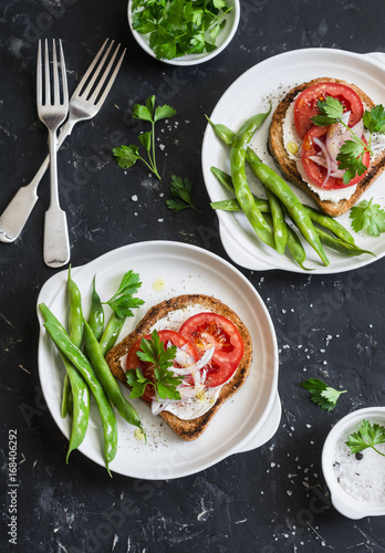 Tomato and cheese sandwiches and green beans is a healthy vegetarian breakfast or snack on a dark table, top view. Flat lay
