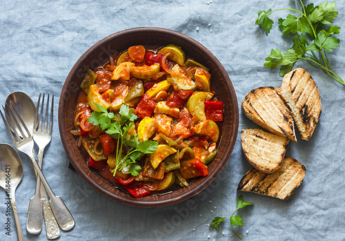 Healthy vegetarian lunch - stewed garden vegetables. Vegetable ratatouille and grilled bread. On a blue background, top view
