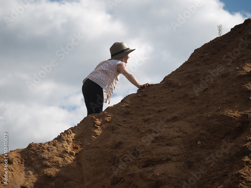 Child is climbing a mountain of sand. A little girl  wearing a hat and barefoot. Journey with the concept of children