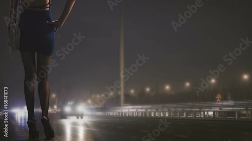 prostitute is standing on the side of the night road where the lanterns are shining and waiting for the client photo