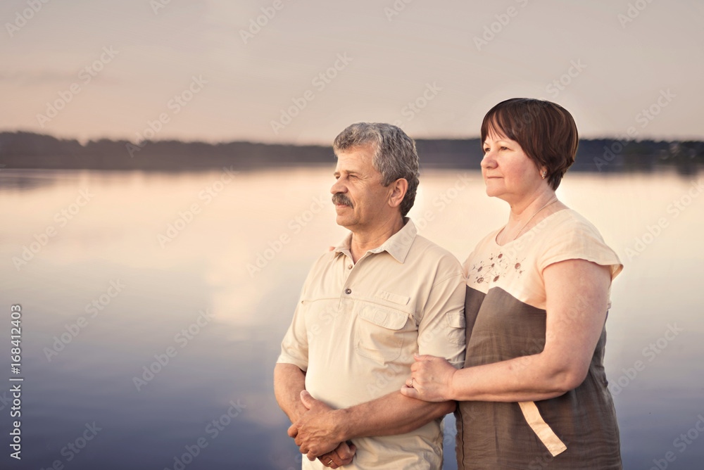 Elderly couple looking at the sunset near the lake river