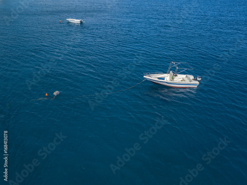 Vista aerea di una barca ormeggiata che galleggia su un mare trasparente. Immersioni relax e vacanze estive © Naeblys