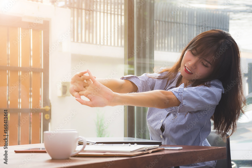 Tired young asian businesswoman is stretching arms after finishing her work at the office or cafe Tired young asian businesswoman is stretching arms after finishing her work at the office or cafe