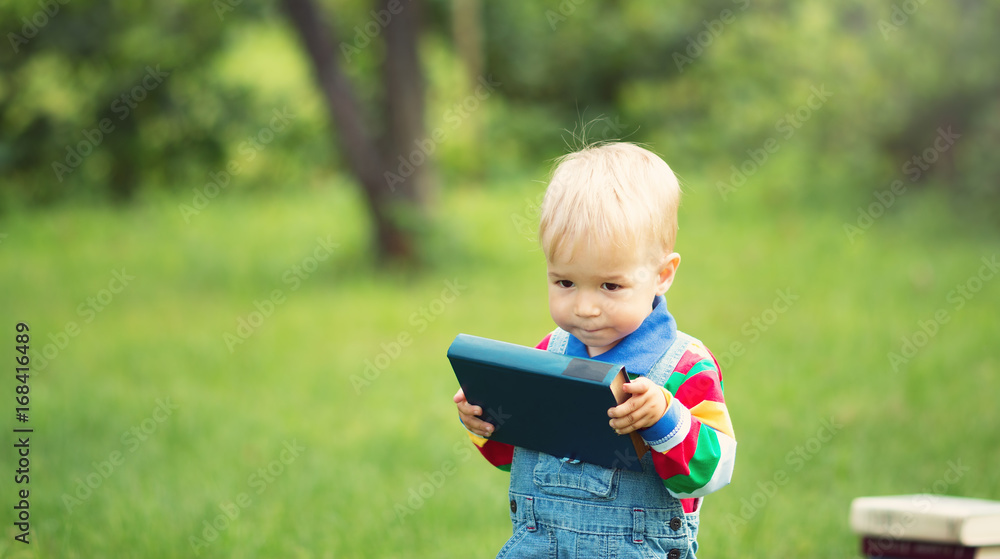 one year old baby reading a book sitting on the grass in garden one year old baby reading a book sitting on the grass in garden