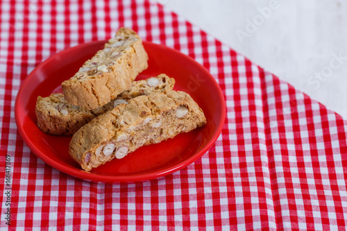 Cantucci. Typical Italian cookies on a saucer of red color and on a white wooden background