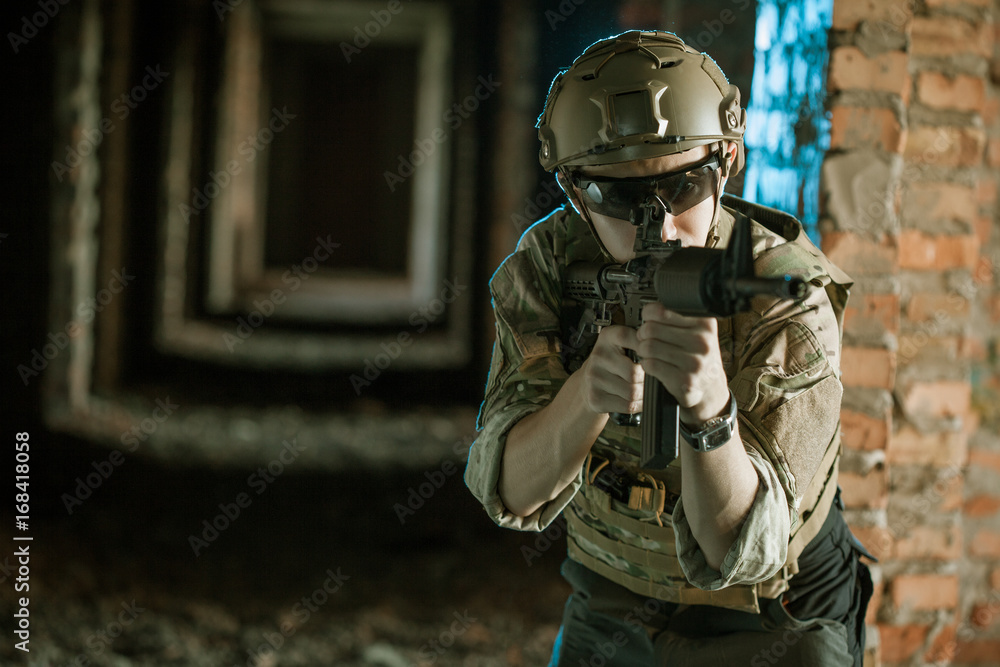 Fototapeta premium airsoft soldier with a rifle playing strikeball In brick building