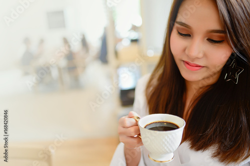 Portrait of beautiful woman holding a cup of coffee in her hand in blur background coffee shop, she drink coffee in the morning, with copy space for text