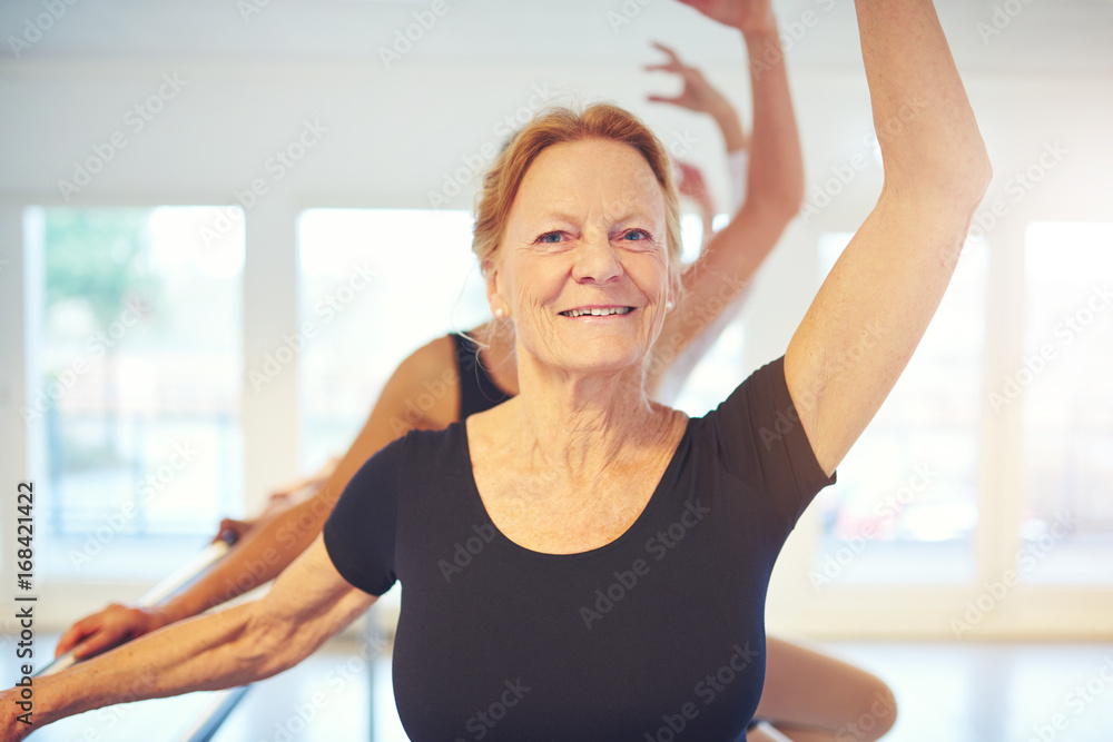 Mature smiling woman standing with hand up in ballet class Mature smiling woman standing with hand up in ballet class