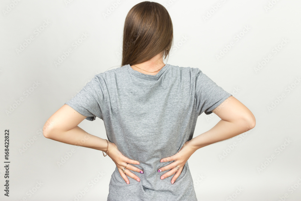 Pretty woman suffers from backache standing over gray background Pretty woman suffers from backache standing over gray background