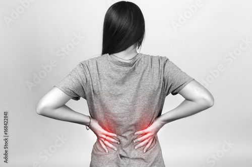  Pretty woman suffers from backache standing over gray background