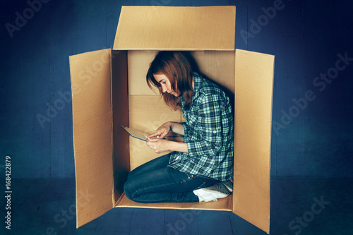 Introvert concept. Woman sitting inside box and working with laptop