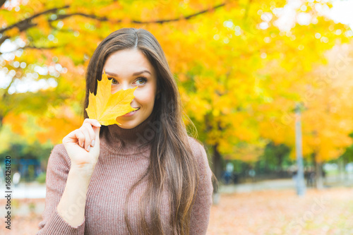 Smiling woman portrait with a yellow leaf in autumn