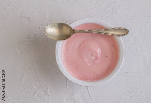 Healthy strawberry fruit flavored yogurt with natural coloring in plastic cup isolated on white rustic background with little silver spoon - top view shot in studio