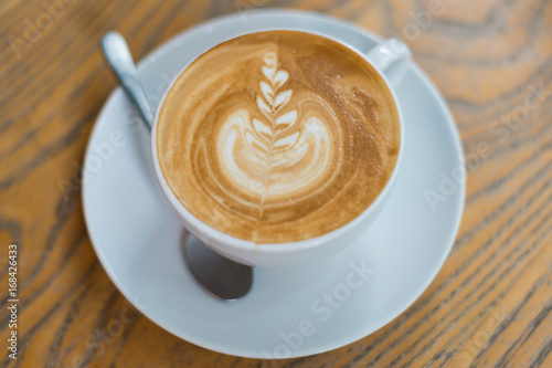 A cup of coffee with flower pattern in a white cup on wooden background