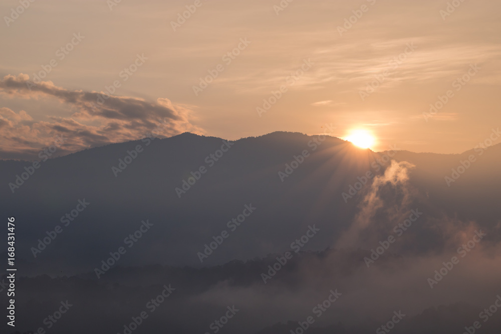 Sunrise behind the mountain with fog in the morning